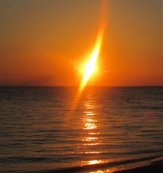 Glaring setting sun casting bright rays on calm waters of warm sea on quiet evening