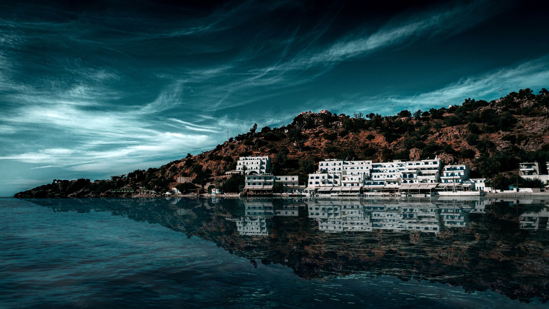 Picturesque view of Loutrón, Greece with white buildings by the Mediterranean sea under a dramatic sky.