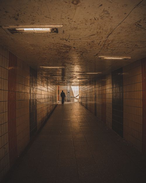 Free Silhouette of a man walking through a dimly lit urban underpass with ceramic tiles. Stock Photo