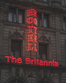 Neon lights of Britannia Hotel sign glowing against historic facade at night in Manchester.