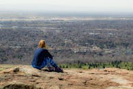 一个女人坐在山岩上，俯瞰着下方的城市和广阔的自然景色，享受着宁静的时刻