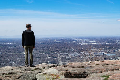 Man Wearing Black Jacket Standing on Rock Monolith