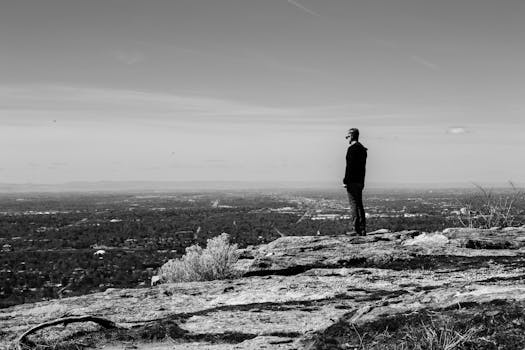 一名男子站在岩石山上，黑白画面中，他凝视着下方广阔的城市景观