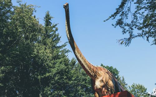 Free A large dinosaur statue in an outdoor park surrounded by greenery and blue sky. Stock Photo