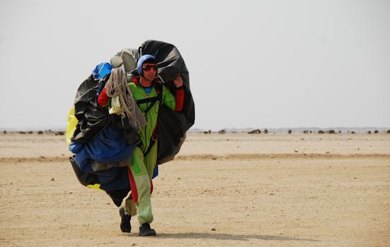 Parachutist in vibrant gear walking across the Namib Desert, carrying parachute equipment.