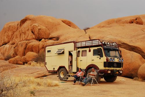 Free A campervan parked in Namibia's arid desert terrain with two adults relaxing outside. Stock Photo
