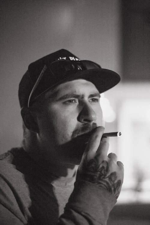 Grayscale Photo of a Tattooed Man Smoking a Cigarette