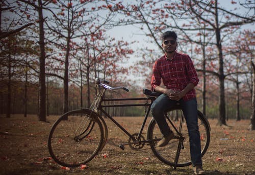 Man Wearing Red Dress Shirt and Blue Jeans Sitting on Black Bicycle