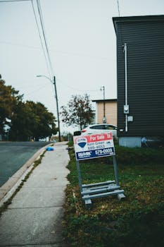 For sale sign outside a suburban house on a quiet street corner.