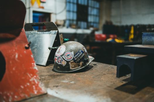 Hard hat with stickers on workbench in an industrial workshop setting.