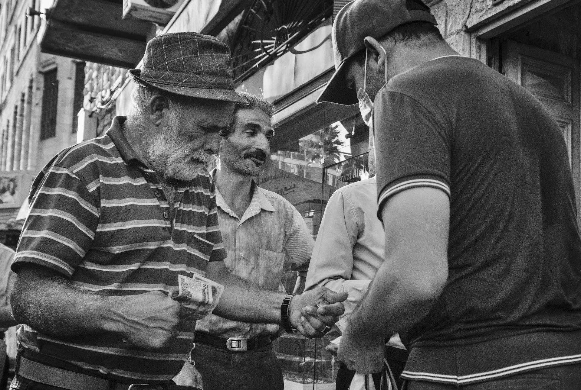 A dynamic street scene of men exchanging money in a busy Amman market, captured in black and white.