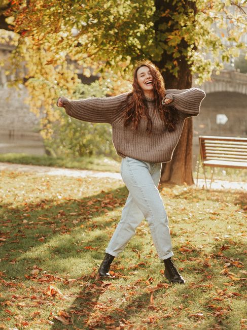 A young woman dancing happily in a sunlit park during autumn, embracing the vibrant season.