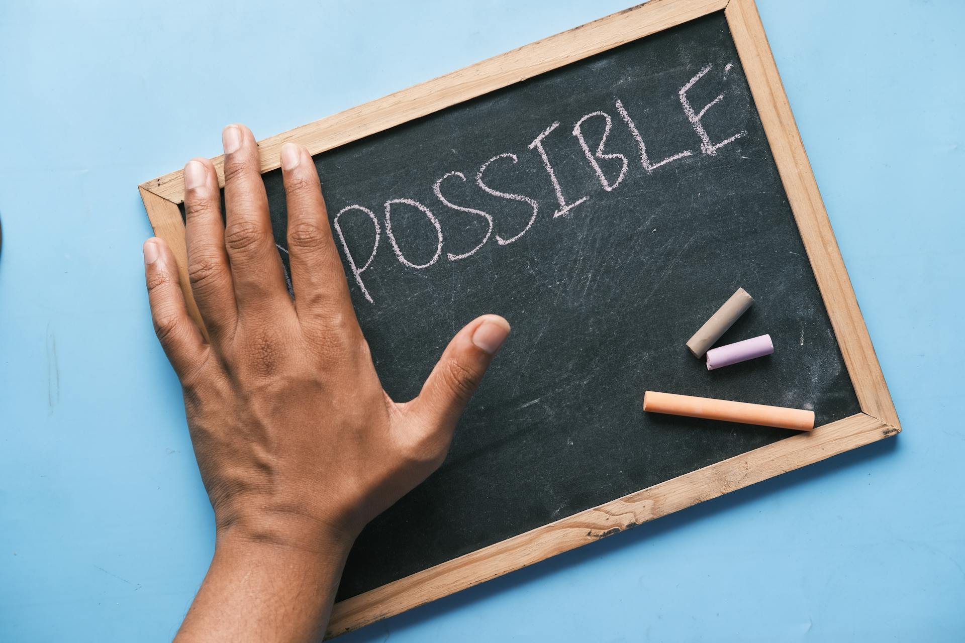 A hand on a chalkboard with 'Possible' written in chalk signifies optimism and potential.