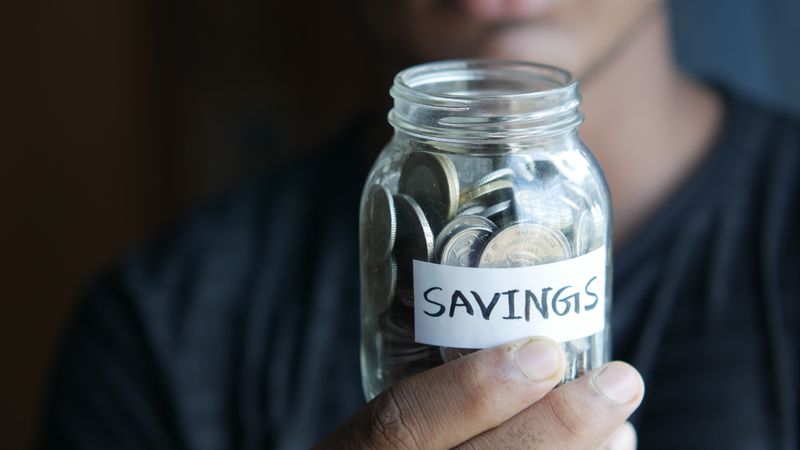 A hand holding a savings jar full of coins.