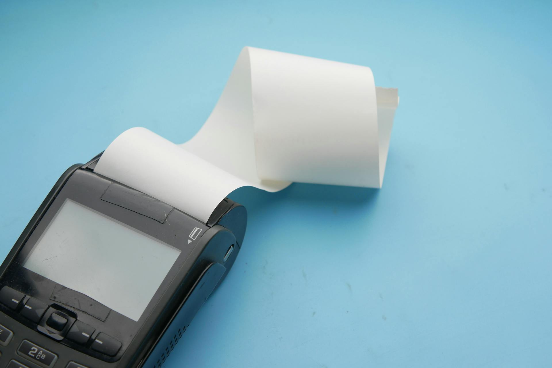 Close-up of a point of sale terminal and thermal paper roll against blue background.