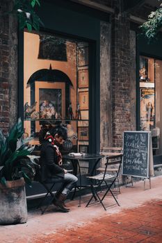 Woman enjoying a peaceful moment reading outside a rustic café with green plants and charming decor.