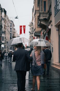 A couple using clear umbrellas walks through a rainy city street. Urban life and weather harmony.