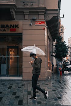 A man walks with a transparent umbrella on a rainy street in a city.