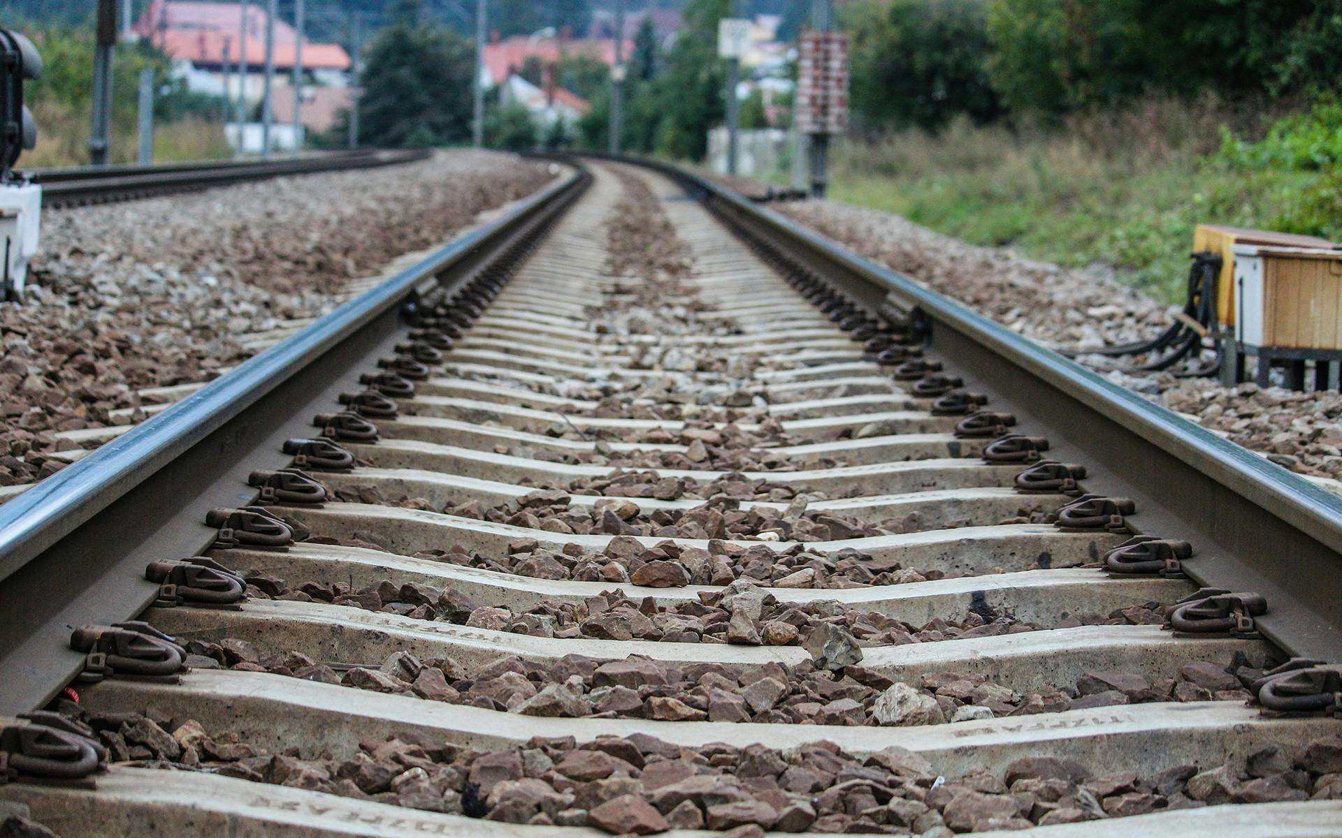 Close view of railway tracks with gravel and greenery in the background, captured outdoors.