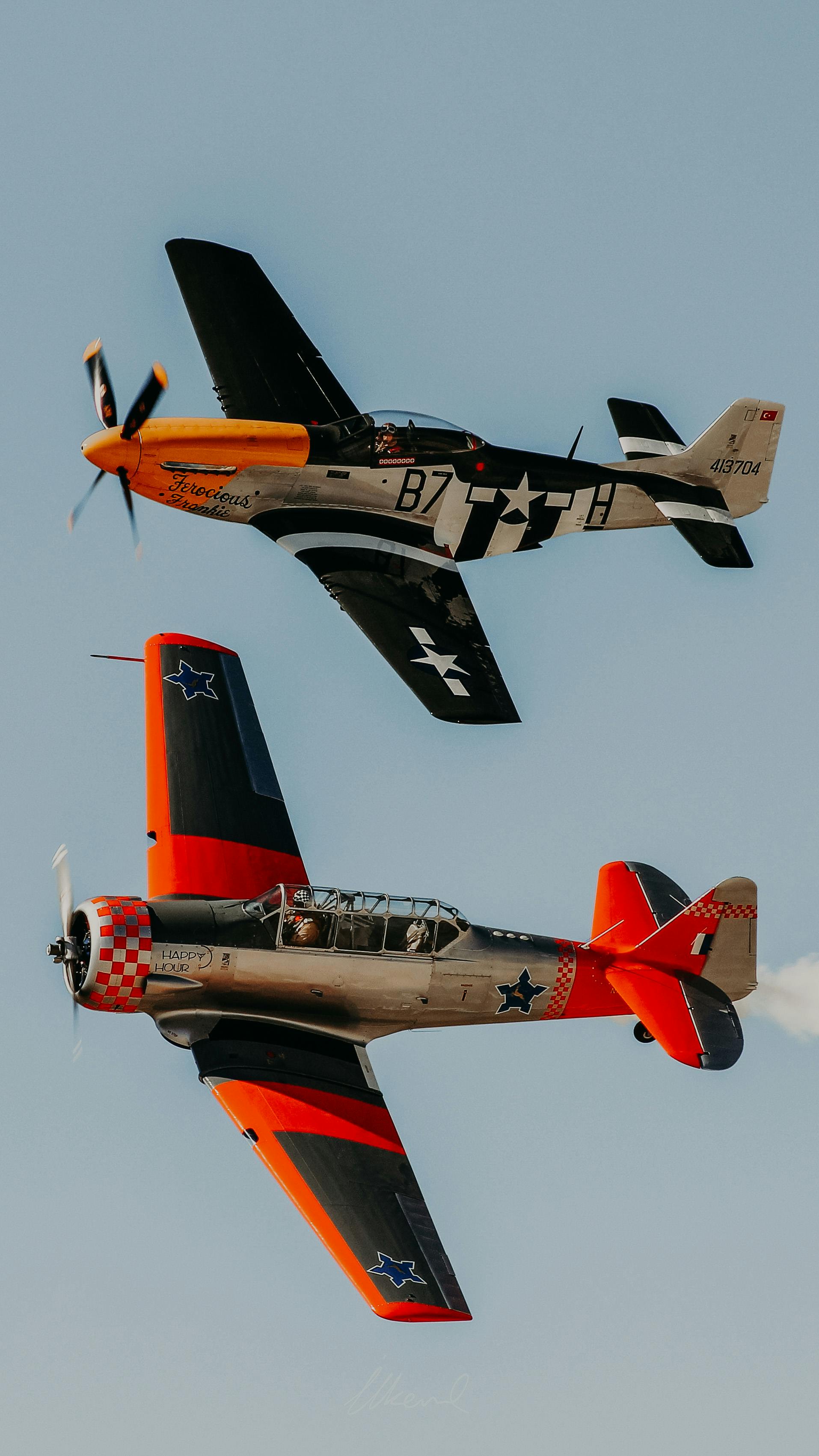 Two vintage military planes in synchronized flight against a blue sky.