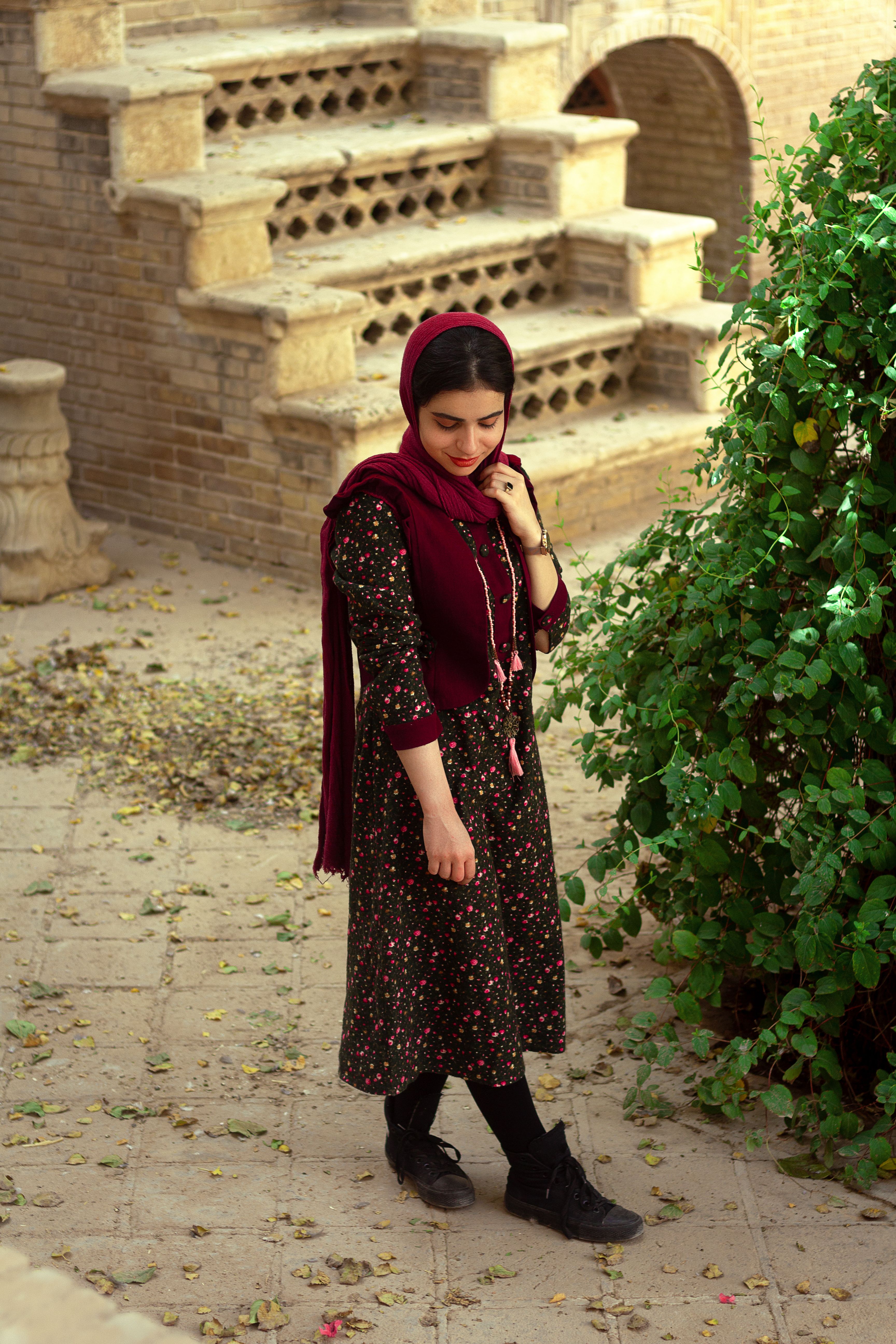 Fashionable woman in burgundy headscarf posing by steps in Tehran.