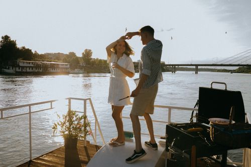 Free A couple enjoys a romantic dance on a yacht during a vibrant sunset with scenic river views. Stock Photo