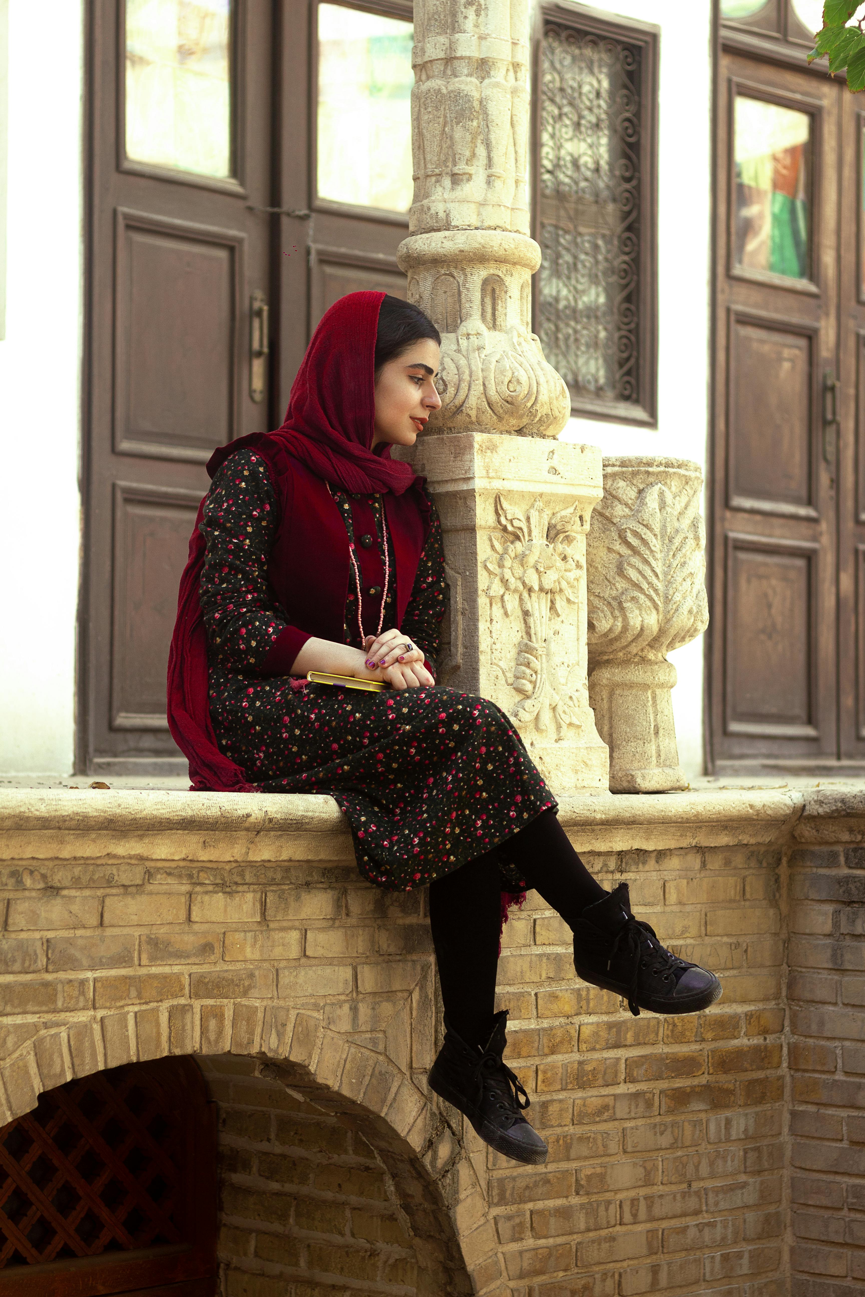Woman in traditional attire sitting on a brick wall outdoors, looking thoughtful.