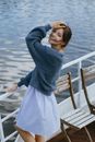 Woman in Blue Sweater and White Skirt Standing on Wooden Dock