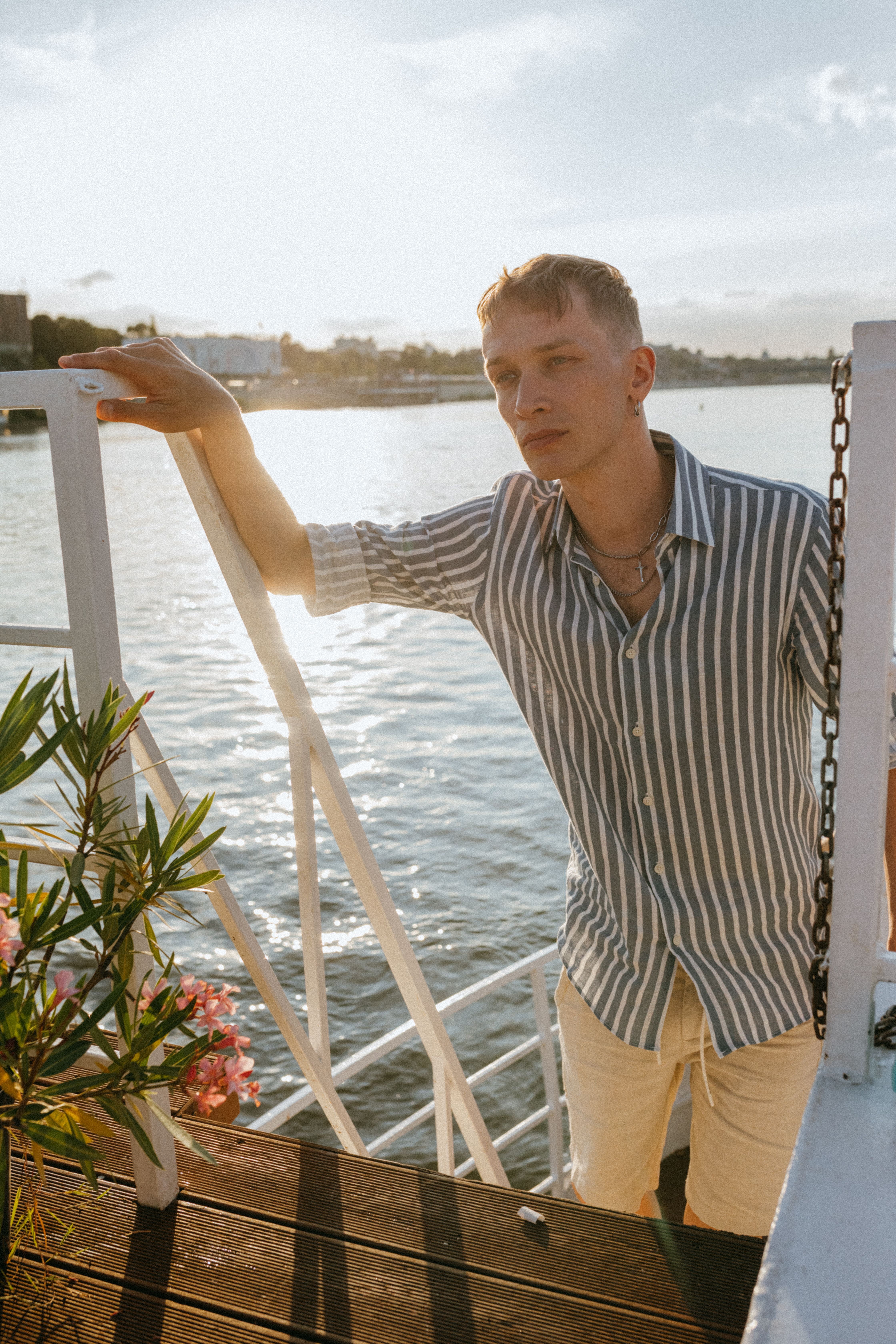 Man standing on a boat in casual attire, enjoying a sunny day by the water.