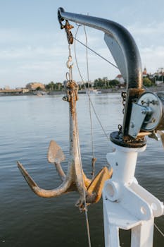 Rusty anchor hanging over a calm harbor, capturing a serene nautical scene.