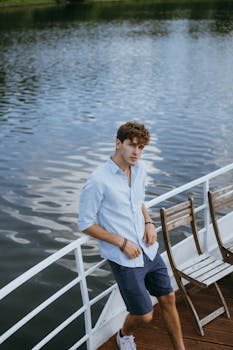 Stylish young man leaning on a boat railing by the tranquil river.