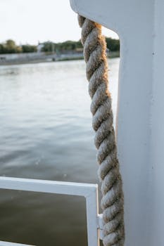 A detailed view of a thick nautical rope on a boat, with a serene river in the background.