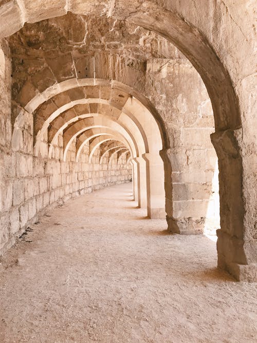 Free Old shabby stone construction with arched empty passage and sandy ground on street on sunny summer day Stock Photo