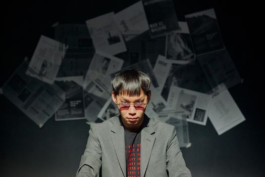 Man in suit with sunglasses in a dimly lit room with papers on the wall.