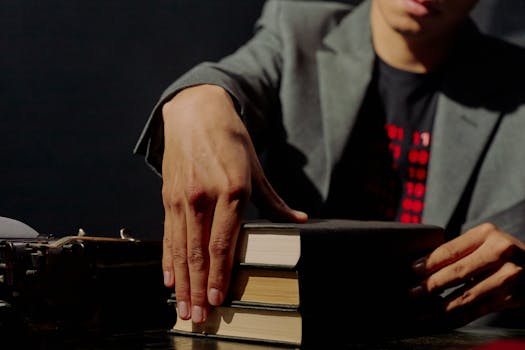 Close-up of a man in a suit placing books on a table with a typewriter nearby in a low-light environment.