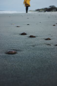 Serene beach scene with scattered stones and a person walking in the distance.