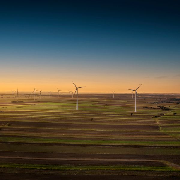 Wind turbines across farmland at sunset — photo by Piotr Arnoldes on Pexels