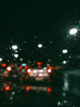 A captivating view of city traffic through a rainy window with bokeh effect, creating a mesmerizing night scene.