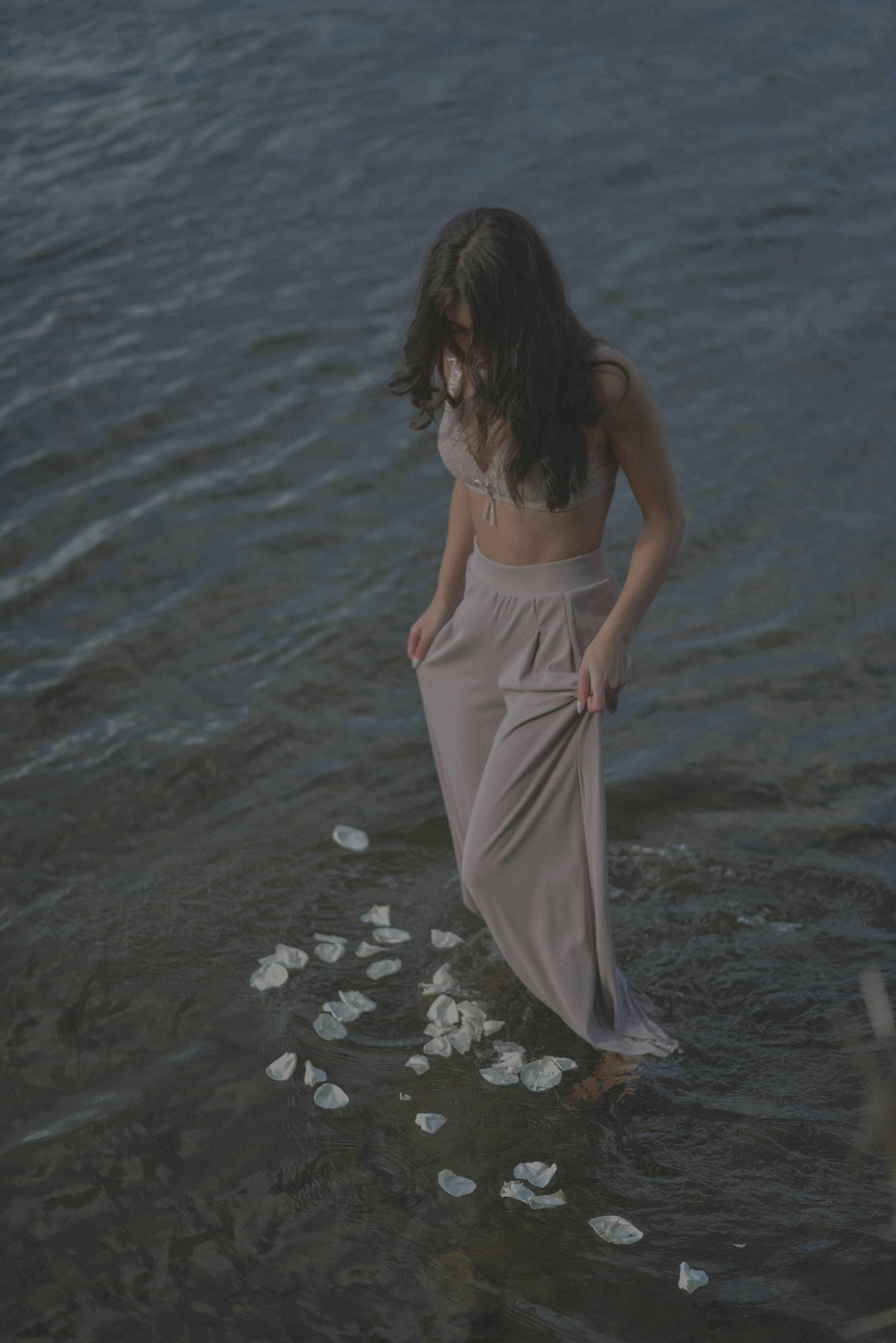 A woman standing in shallow water surrounded by floating petals, creating a serene scene.