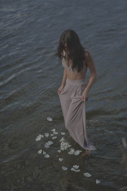 A woman standing in shallow water surrounded by floating petals, creating a serene scene.