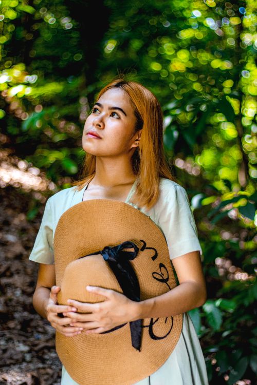 Free A young woman holds a sun hat, gazing upwards in a serene forest setting. Stock Photo