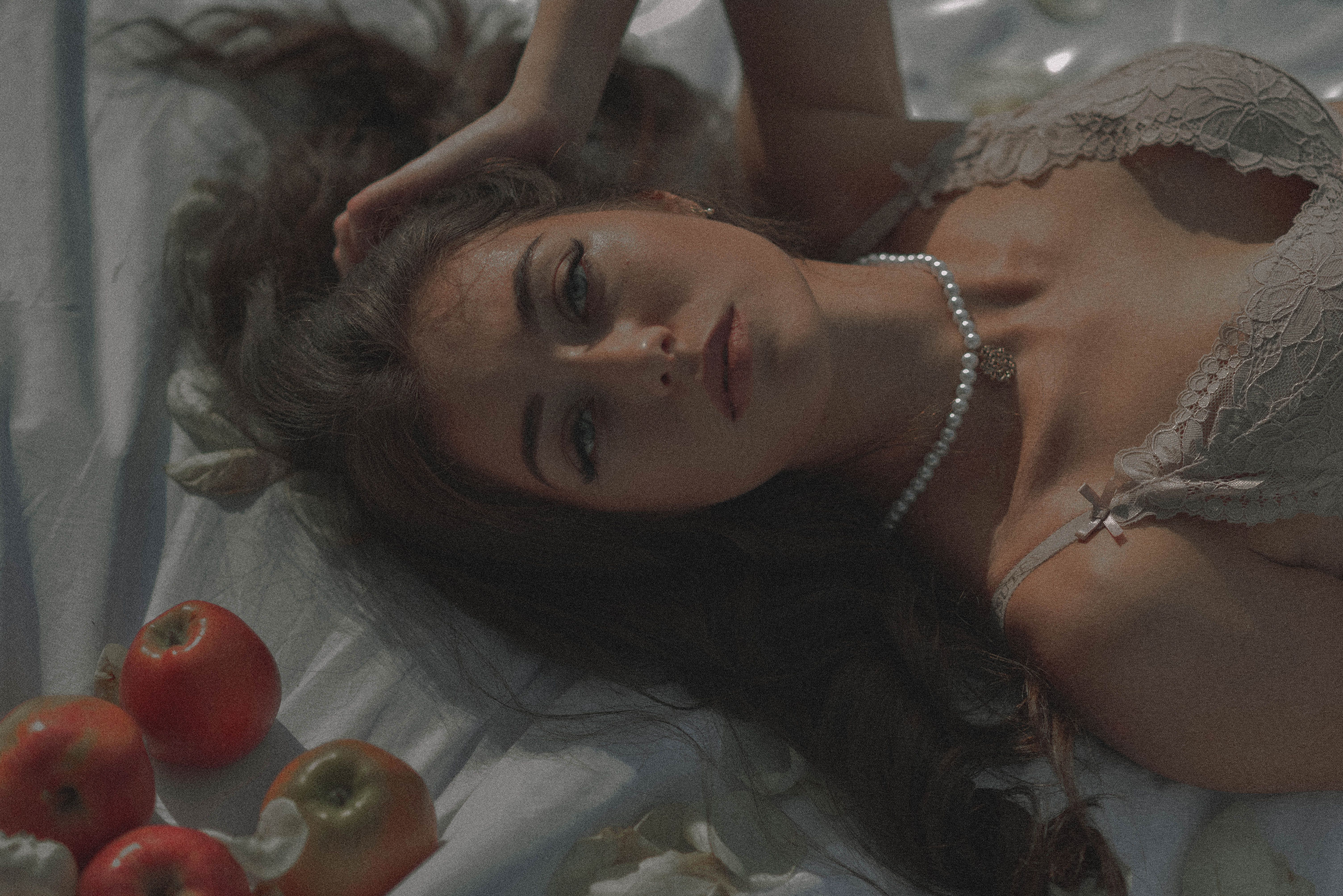 A woman lying gracefully in lace lingerie, surrounded by apples, exuding elegance and allure.