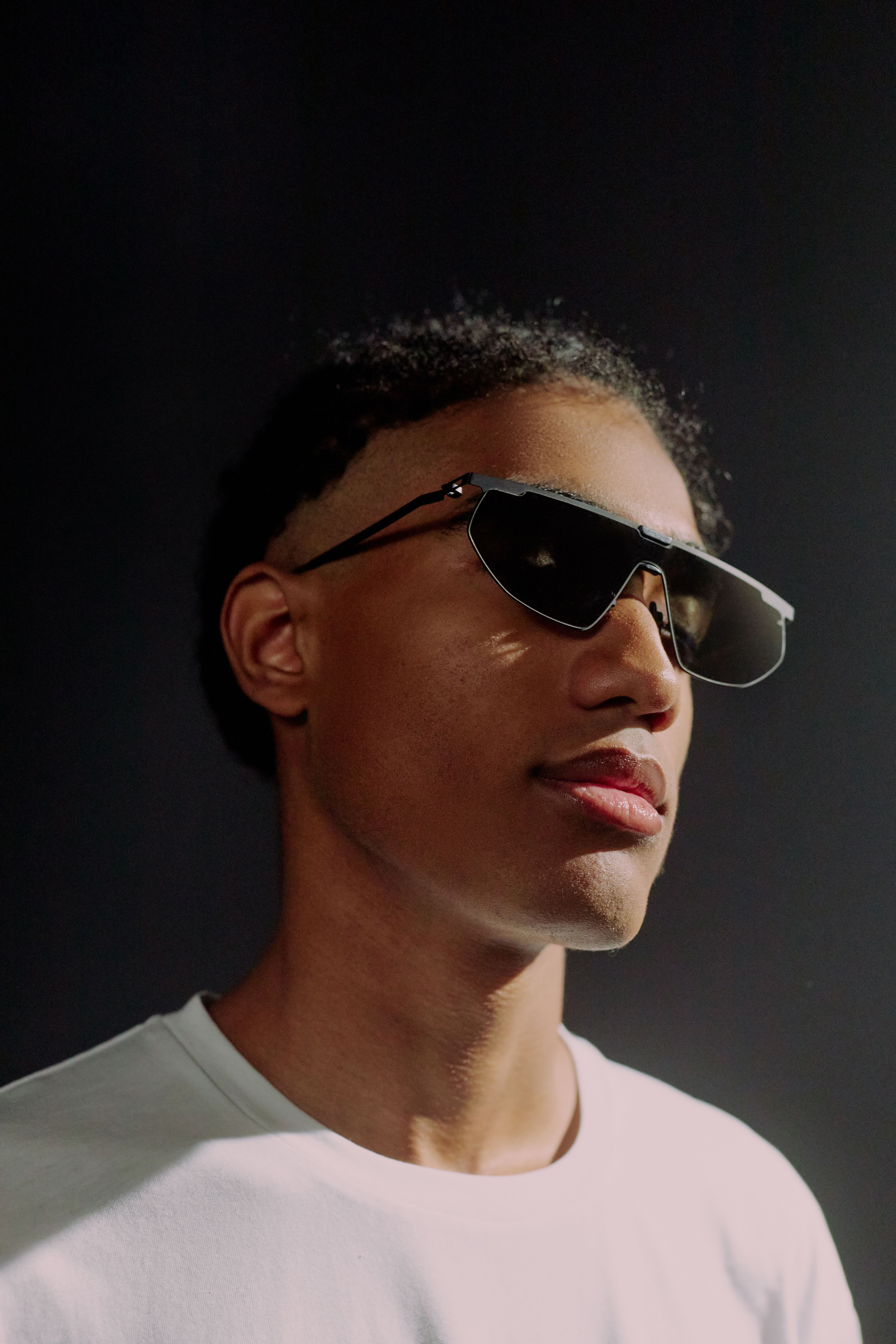 Studio portrait of a fashionable man in sunglasses against a dark background.