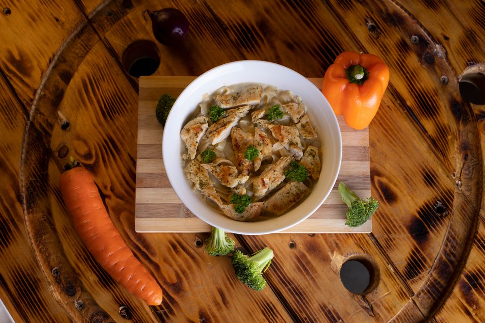 Chicken and vegetable soup in a white bowl on a wooden table
