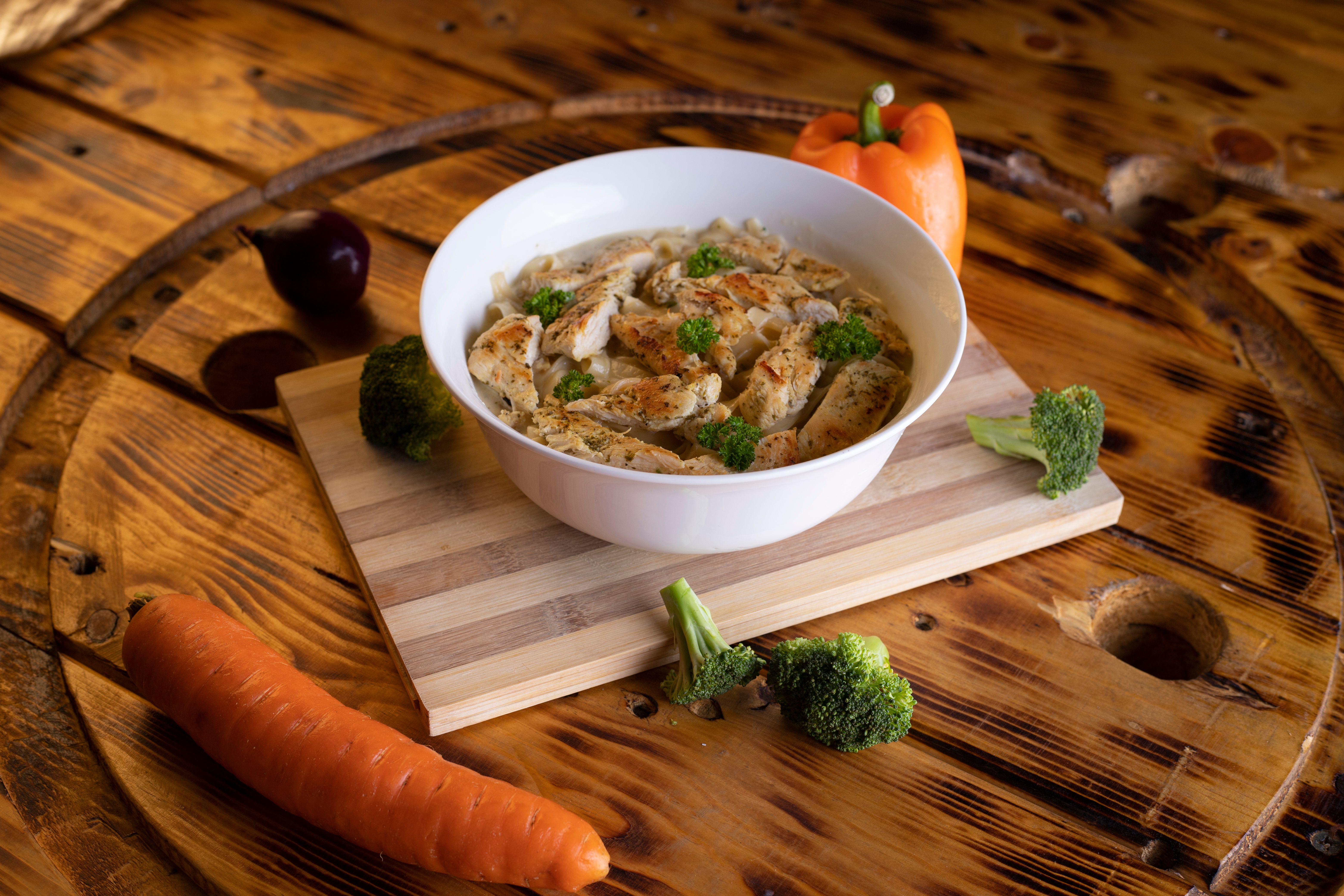 Free A hearty chicken soup with vegetables, beautifully presented in a white bowl on a rustic wooden table. Stock Photo