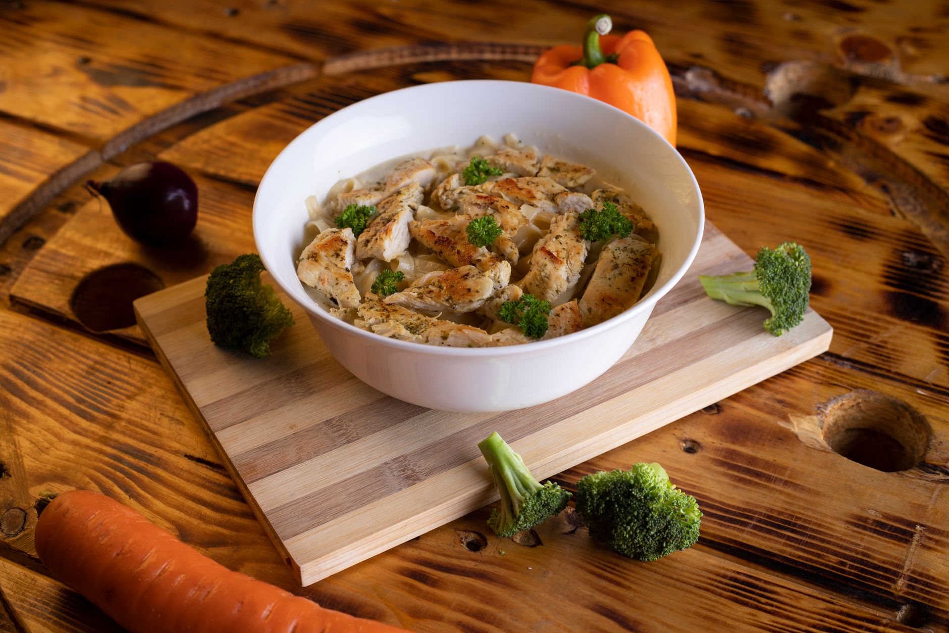 A bowl of creamy rasta pasta with golden jerk chicken strips, vibrant red and yellow bell peppers, and penne noodles coated in rich coconut cream sauce