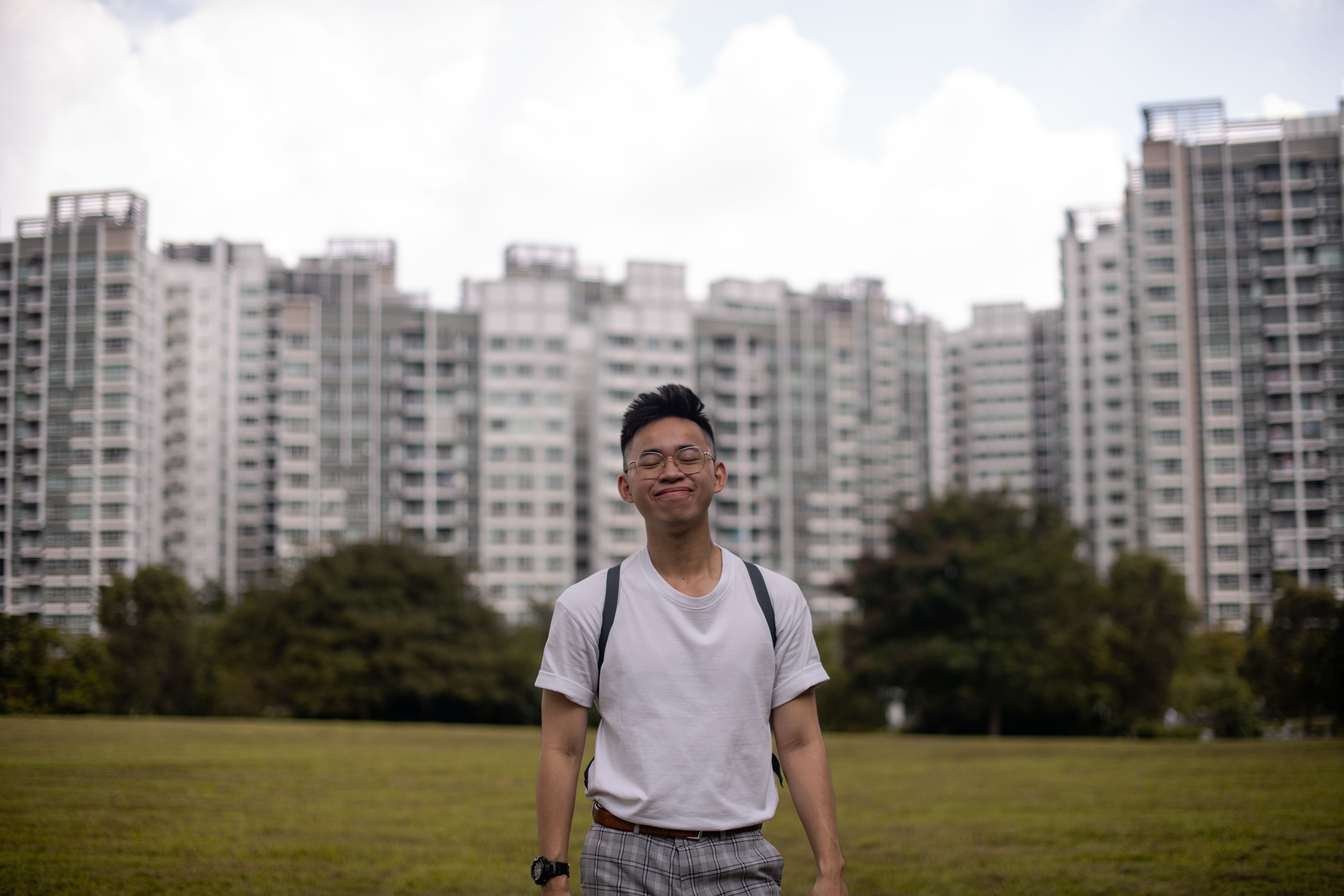 Young man smiling with eyes closed, standing outdoors in front of city skyline.