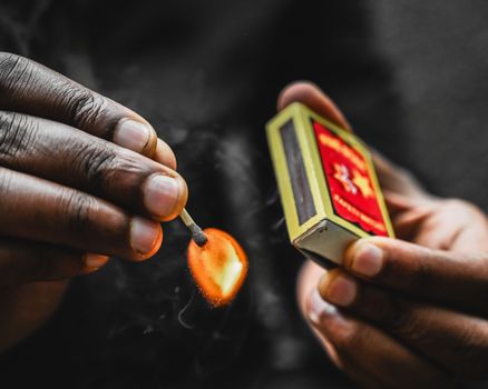 A detailed close-up of hands igniting a matchstick, showcasing the flame and action.