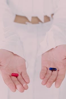Close-up of hands holding red and blue pills, symbolizing choice in a minimalist setting.