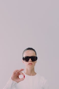 Woman with sunglasses holding a red pill in a minimalist studio setting.